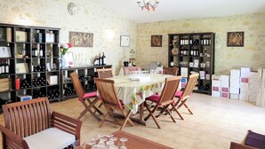 A dining area with a long table set for six, surrounded by wooden chairs with cushioned seats. There are wine bottles and glasses on shelves against the walls.