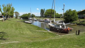 A riverside marina with boats docked along the water, grassy banks, and a clear blue sky.