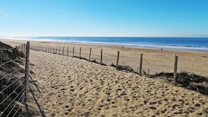 En sandstig som löper längs stranden, med ett trästaket som leder ner till havet.