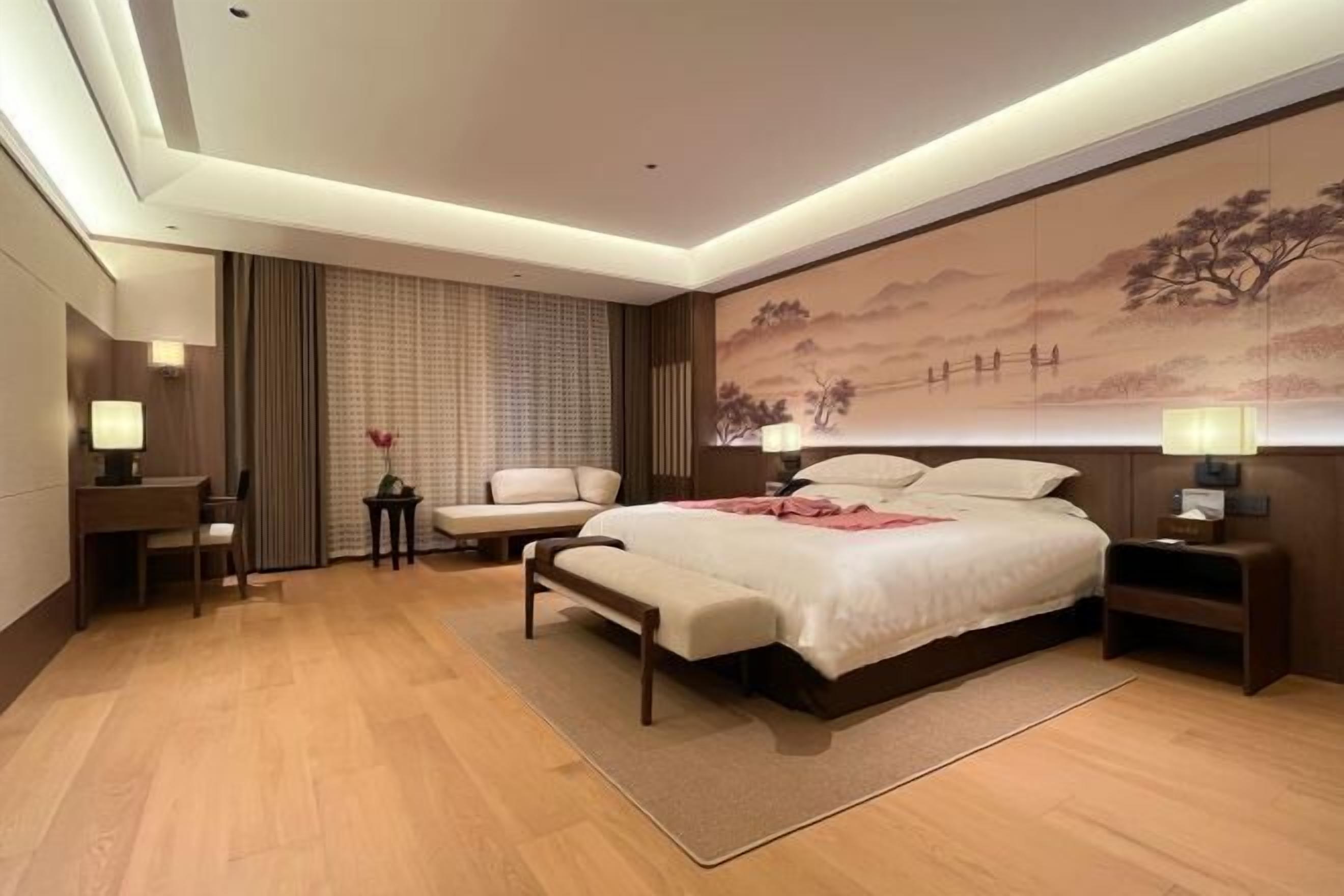 A hotel room with a large bed, a desk, a chair, and a small table with a vase of flowers.
