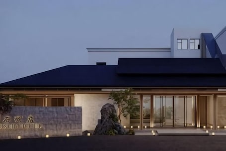 A modern hotel with a stone facade, large windows, and a well-lit entrance.. Baoshi Hotel