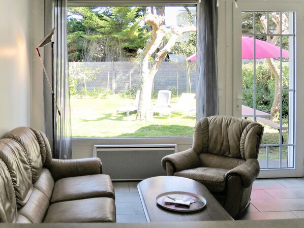 A room with two leather armchairs, a small table with a tray, and a large window offering a view of a backyard with a tree, chairs, and a fence.