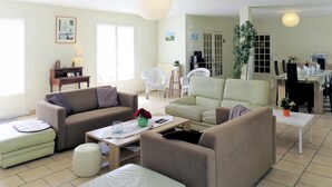 Amplia sala de estar con un juego de sofás, una mesa de comedor y una cocina a la vista al fondo.
