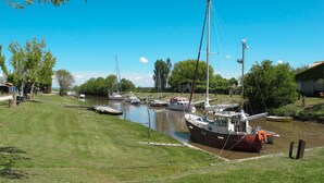 Marina a orillas del río con barcos amarrados, orillas cubiertas de hierba y un cielo azul despejado.