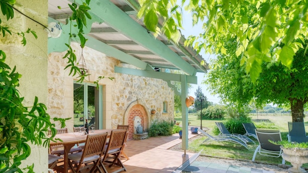 An outdoor patio with a stone wall, a brick oven, and a table with chairs. - Babelle by Interhome (Gaillan-en-Médoc)