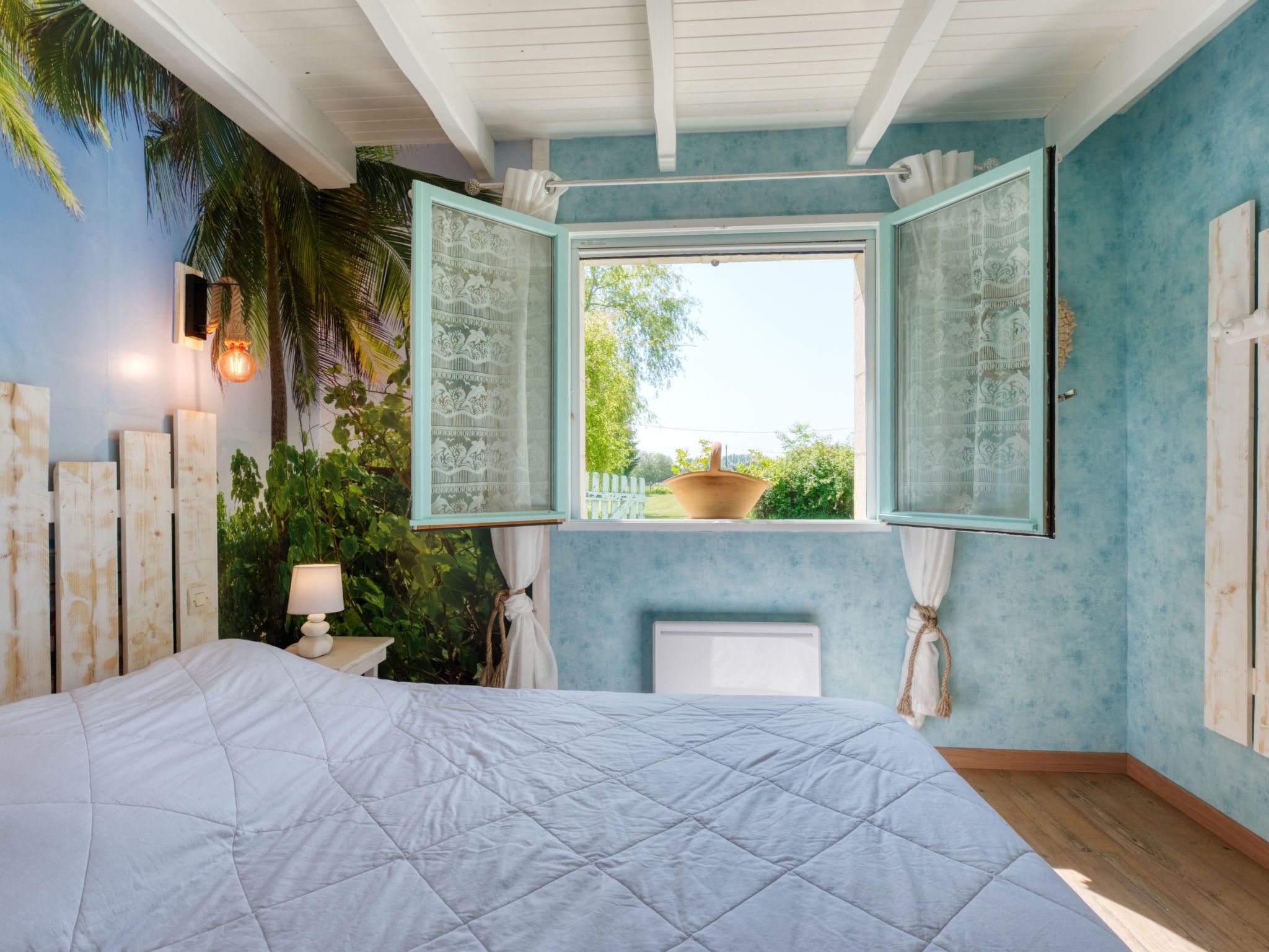 Ein Schlafzimmer mit einem großen Bett, einem Fenster mit geöffneten Fensterläden und Blick auf Grünfläche.
