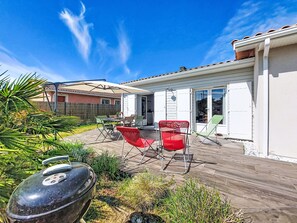 Un patio con mobiliario exterior, una parrilla de barbacoa y un edificio blanco con tejado de tejas.