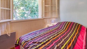 Un dormitori amb una finestra gran, un llit amb un llençol de llit de colors i teules de fusta al sostre.