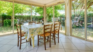 Zona de porxo coberta amb taula preparada per dinar, envoltada de grans finestres de vidre que donen vistes a un jardí.