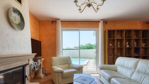 Un salon avec une cheminée, un canapé, un fauteuil et une table basse. Une grande fenêtre offre une vue sur l’extérieur.