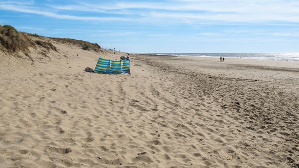 Une plage de sable avec un parasol rayé et une dune en arrière-plan.