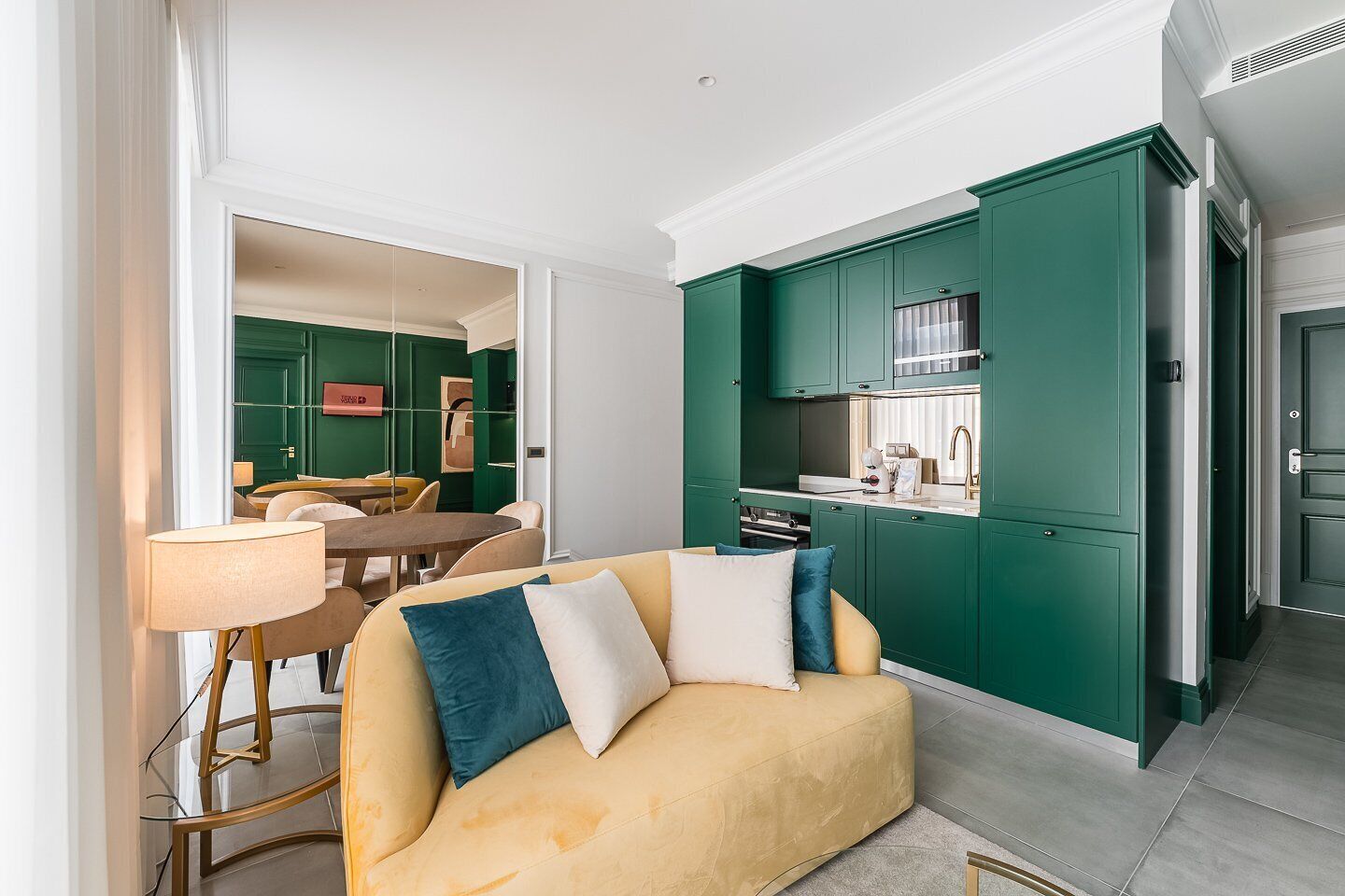 Sala moderna com sofá, mesa de jantar e cozinha com armários verdes.