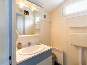 Une salle de bain avec un lavabo blanc, un miroir et une fenêtre située au-dessus des toilettes.