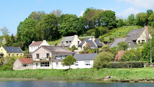 Un pittoresco villaggio sul fiume, con case costruite su una collina, caratterizzato da un mix di stili architettonici e un fiume tranquillo in primo piano.