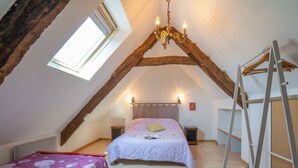 A bedroom with a sloped ceiling, a bed with a floral bedspread, a small bedside table, a nightstand, and a wooden ladder. - Les Azalées by Interhome (Ploumilliau)