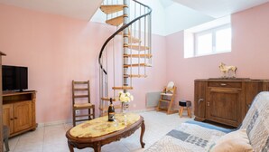 A cozy room with a spiral staircase, a wooden cabinet, a television, and a comfortable seating area with a patterned rug. - Les Azalées by Interhome (Ploumilliau)