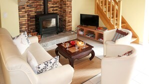 A living room with a brick fireplace, a television, and a wooden staircase. - Entre Terre et Mer by Interhome (Ploumilliau)
