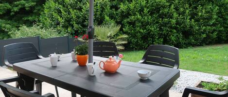 Um pátio externo com uma mesa posta para dois, rodeado por cadeiras e um vaso de planta.