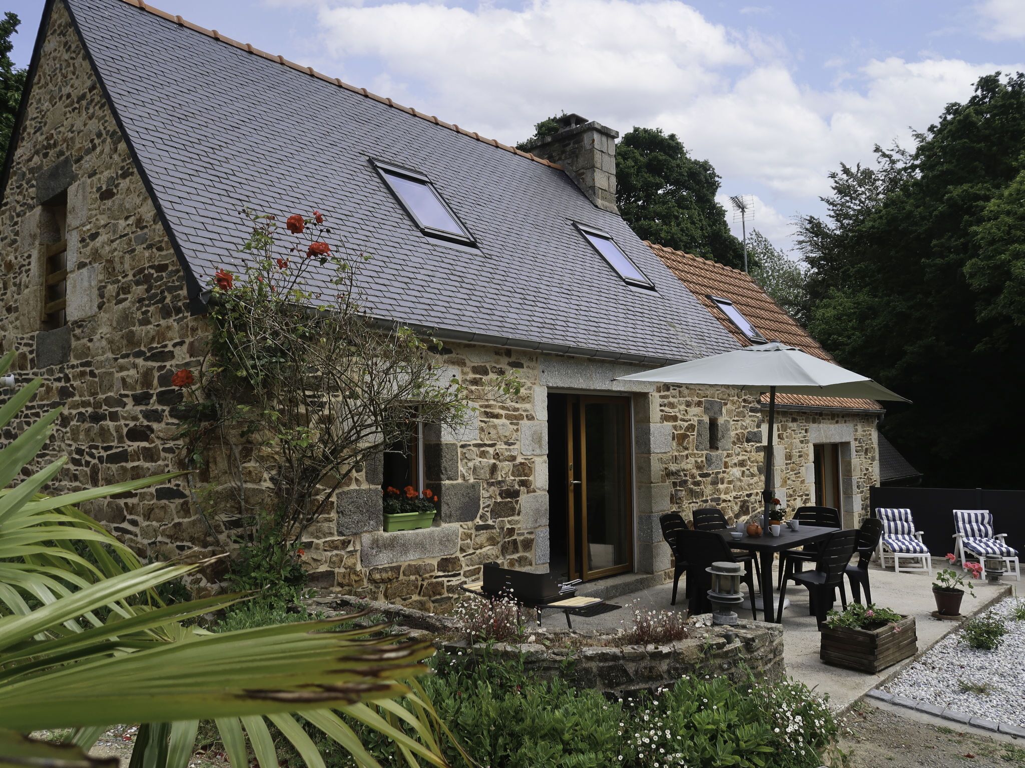 Una casa de piedra con techo inclinado, un patio amoblado y un jardín.