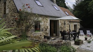 A stone house with a sloped roof, a patio with outdoor furniture, and a garden area. - Entre Terre et Mer by Interhome (Ploumilliau)