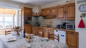 A kitchen with wooden cabinets, a dining table set for four, and a view of the sea through the window. - Blaues Meer by Interhome (Plouarzel)