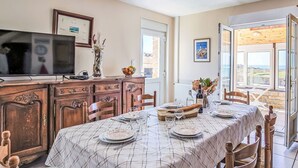 A dining area with a table set for four, a television, and a view of the countryside through large windows. - Blaues Meer by Interhome (Plouarzel)