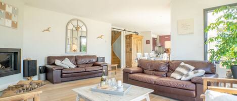 A spacious living room with two brown leather sofas, a white coffee table, and a wooden TV stand.