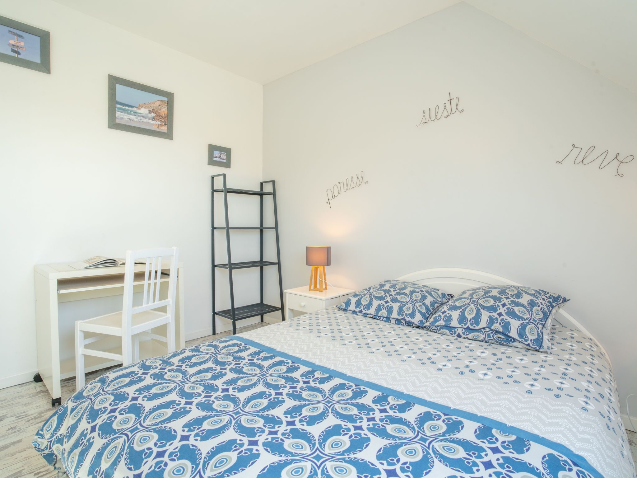 Ein Schlafzimmer mit einem Bett, einem Schreibtisch, einem Stuhl, einer Leiter und einer Wand mit dekorativem Text.