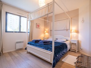 Ein Himmelsbett mit weißem Gestell und blauer Bettwäsche, zwei Nachttischlampen, ein kleiner Nachttisch und ein Heizkörper.