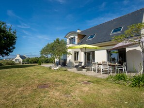 Ein modernes Haus mit Terrasse, Sitzgelegenheit im Freien und Blick auf das Meer.