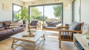 A spacious living room with a brown leather sofa, a wooden coffee table, and two armchairs. Large windows provide a view of the outdoors. - Vacation home Hidel by Interhome (Plouarzel)