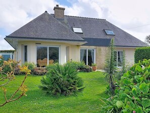Une maison à deux étages, dotée d’un toit en pente, de grandes fenêtres et d’un jardin bien entretenu.