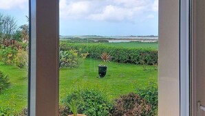 A view through a window of a lush garden with a large planter, a grassy lawn, and distant hills.
