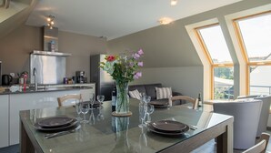 Une cuisine moderne avec un coin repas, comprenant une table en verre, un vase de fleurs et une vue dégagée grâce à de grandes fenêtres.