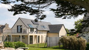 Une maison moderne à deux étages, dotée d’un toit en pente, d’un balcon avec une balustrade et d’une cour arrière clôturée.