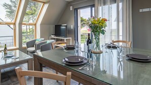 Un coin repas avec une table en verre, des chaises et un téléviseur en arrière-plan.