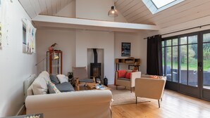 Un vaste salon doté d’un haut plafond, d’un plancher en bois, d’une lucarne, d’une cheminée et d’une grande fenêtre offrant une vue sur l’extérieur.
