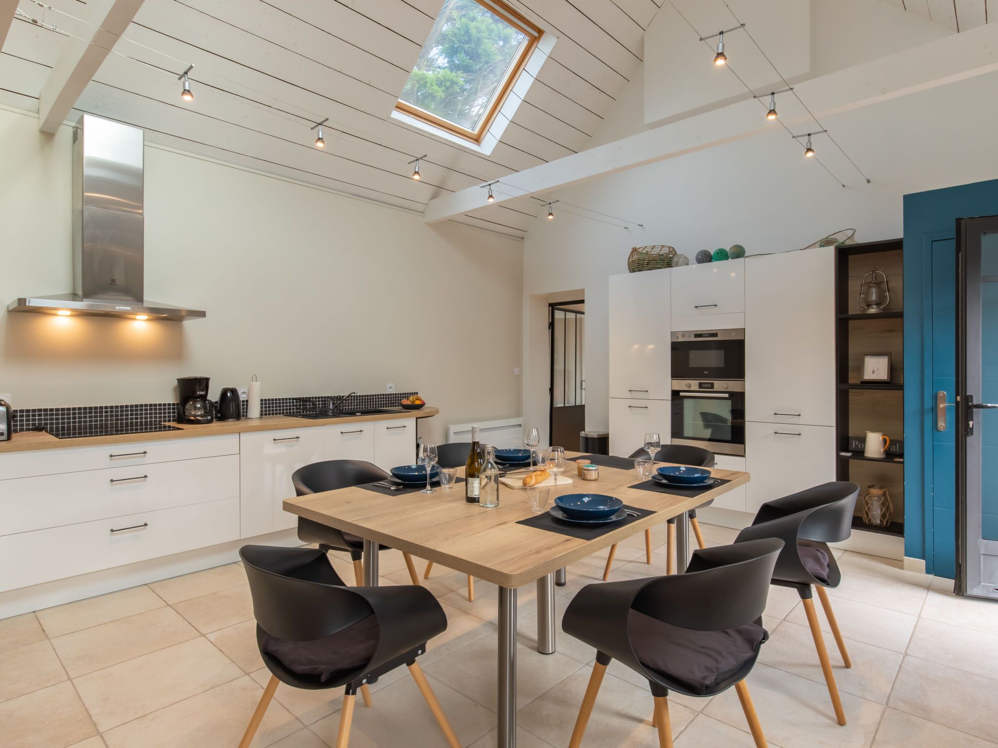 A modern kitchen with a dining area, featuring a wooden table, black chairs, and a skylight above.