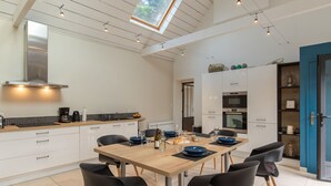 Une cuisine moderne avec un coin repas, comprenant une table en bois, des chaises noires et une lucarne au-dessus.