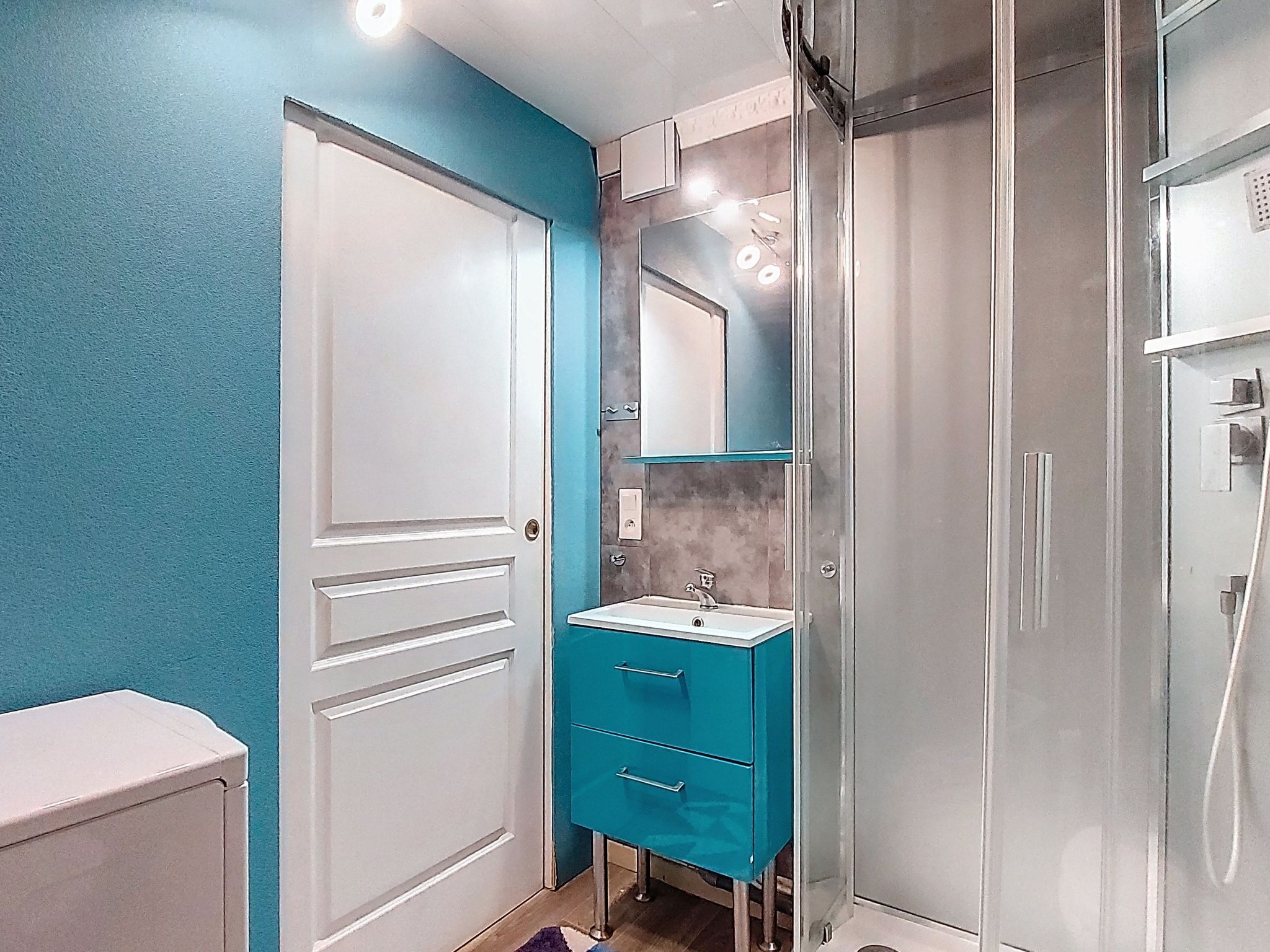 Ein Badezimmer mit weißer Tür, einem blauen Schrank, einem Spiegel und einer Duschkabine.