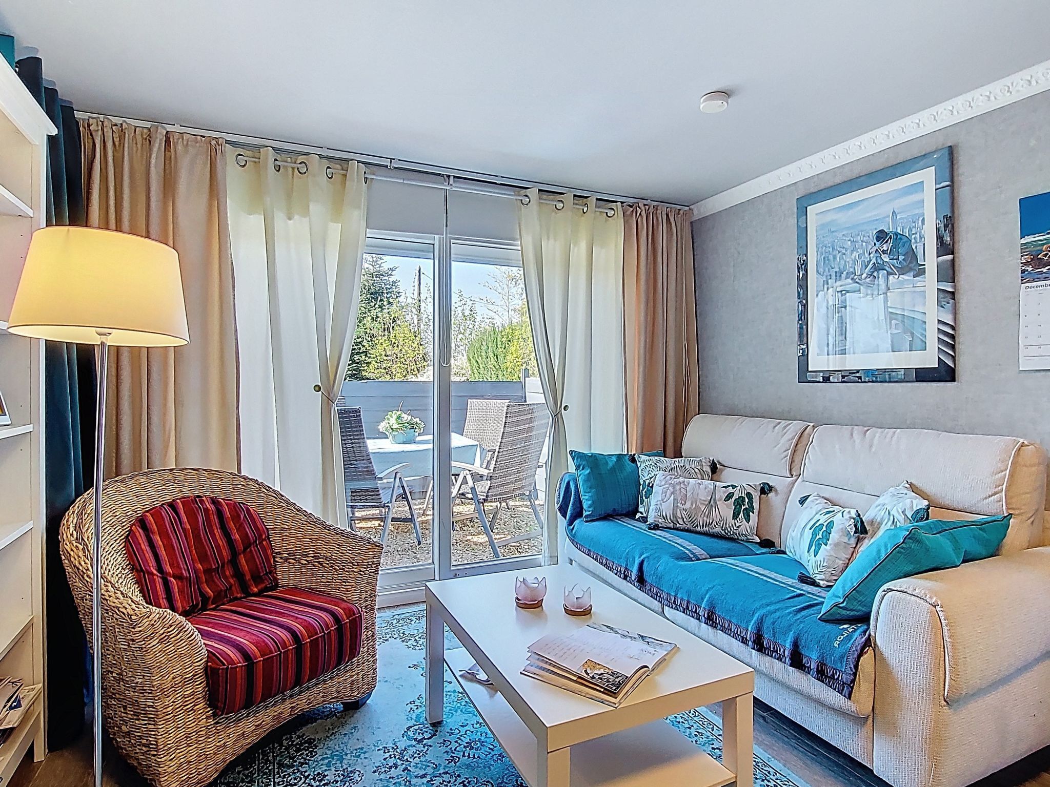 Un salon comprenant un canapé, un fauteuil, une table basse et une porte vitrée donnant sur un espace extérieur aménagé avec une table et des chaises.