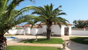 A courtyard with a swimming pool, palm trees, and a building with a tiled roof. - Memphis by Interhome (Miami Platja)