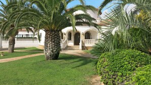 A white building with a tiled roof, surrounded by palm trees and a well-maintained lawn. - Memphis by Interhome (Miami Platja)