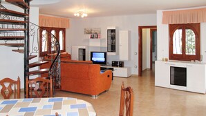 A spacious living area with a dining table, orange sofa, and a TV. A spiral staircase leads to an upper level. - Memphis by Interhome (Miami Platja)