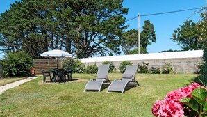 Un jardin avec une terrasse, deux chaises longues, une table avec des chaises et un petit abri de jardin.