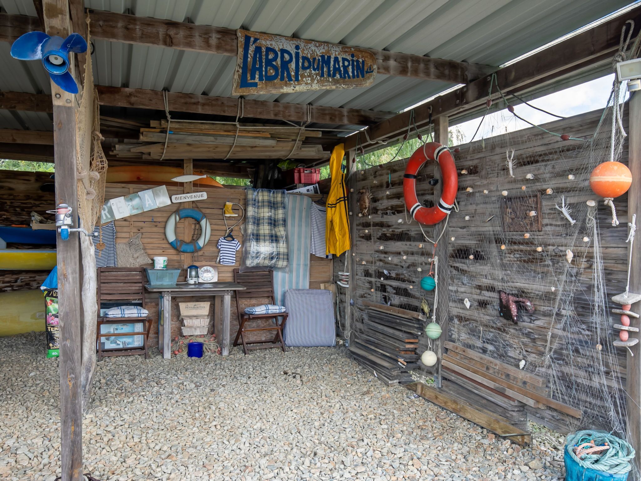 Une cabane rustique avec un intérieur en bois, une enseigne indiquant « LABRIMARIN », et divers objets de marine, comme des bouées de sauvetage et des filets de pêche.