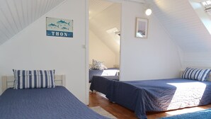 Ein gemütliches Schlafzimmer im Dachgeschoss mit zwei Betten, Holzboden und schrägem Giebeldach.
