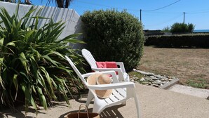 A white plastic chair with a straw hat and a woven basket on a concrete surface.