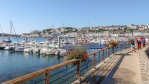 A marina with boats docked, a stone walkway, and a town in the background.