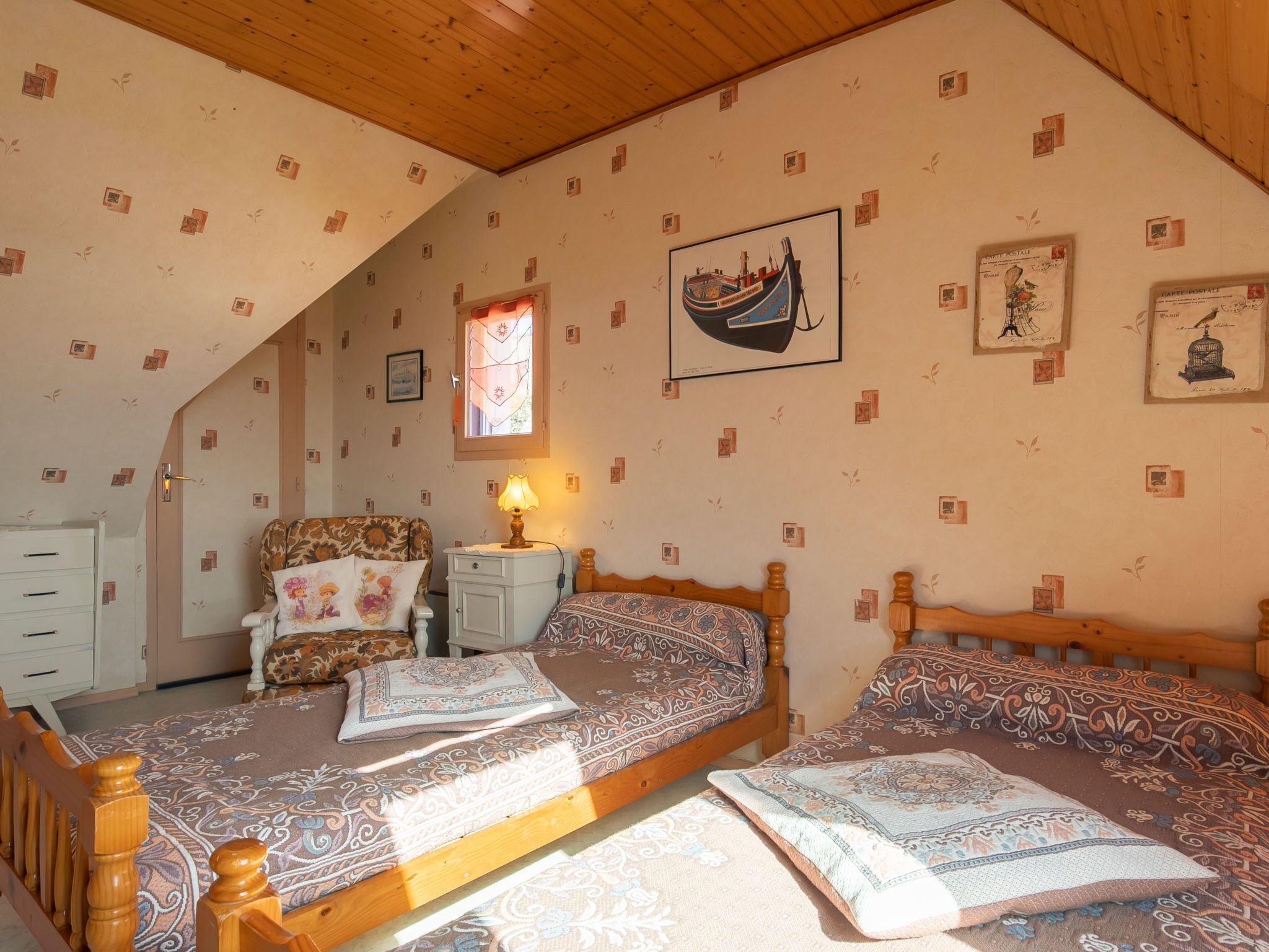 Une chambre avec deux lits, une table de chevet, une chaise et une fenêtre donnant sur un bateau.